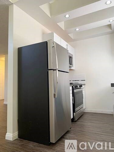 A black refrigerator stands in a kitchen with a stainless steel oven and microwave.