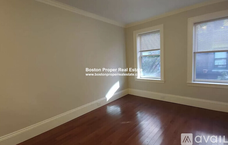 A room with wooden flooring and two windows, with a website address for Boston Proper Real Estate.