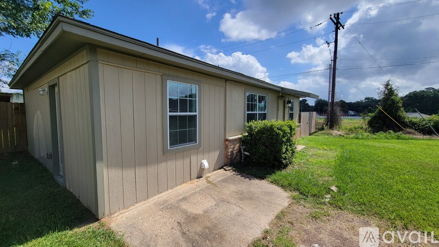 A small house with a brown siding and a white door is surrounded by a grassy area and a dirt path.