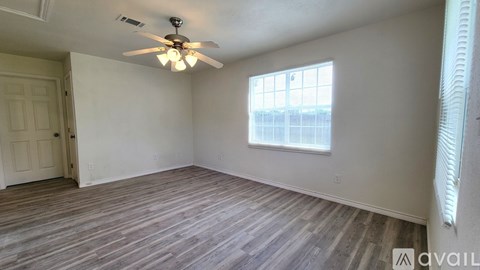 A kitchen with a sink, stove, and refrigerator in a room with wooden flooring and white walls.
