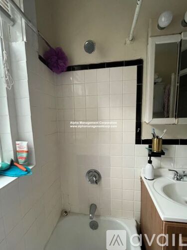 A white tiled bathroom with a shower, sink, and mirror.