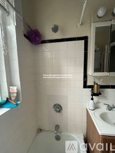 A white tiled bathroom with a shower, sink, and mirror.