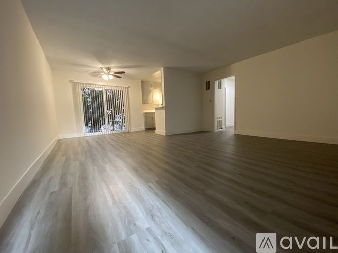 A spacious room with wooden flooring and a window with blinds.