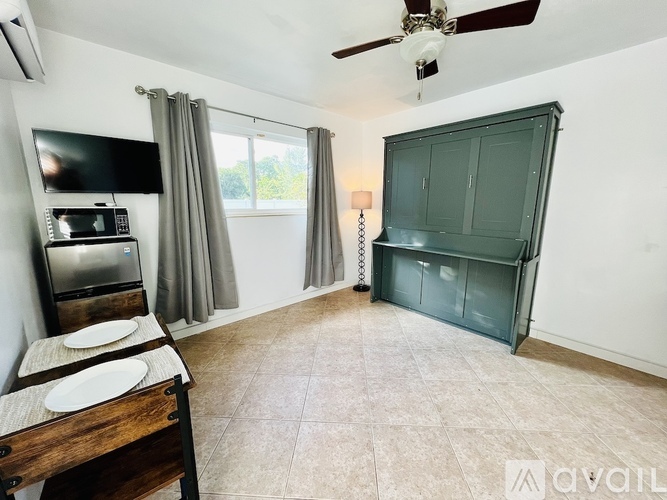 A room with a ceiling fan, a microwave, a refrigerator, a cabinet, and a window with curtains.