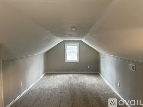 A spacious attic room with a window and carpeted floor.
