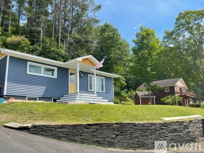 A blue house with a flag on the roof is surrounded by greenery.