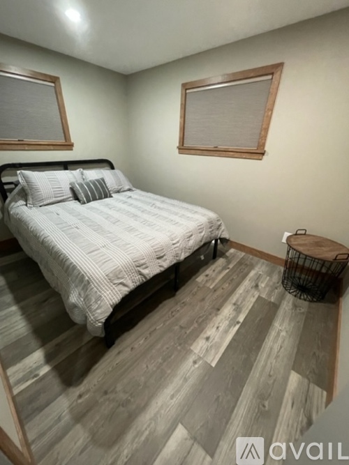 A bedroom with a bed, a small table, and two windows.