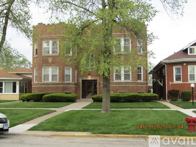 A tree in front of a brick building with bushes on the lawn.