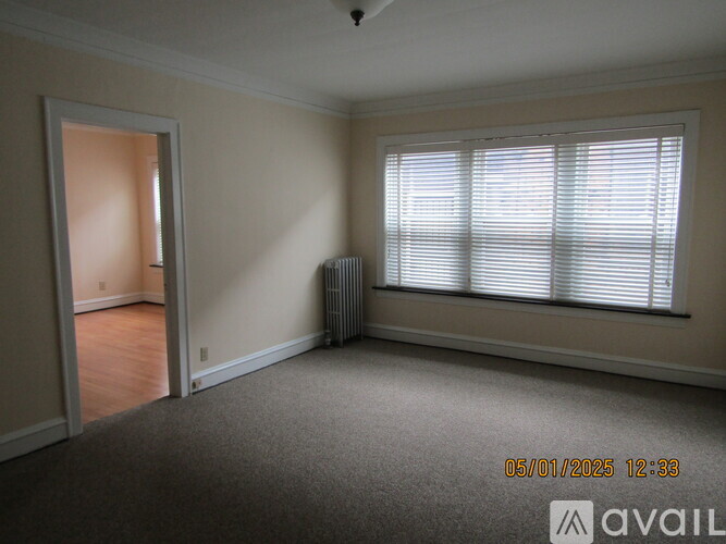 A room with a carpeted floor, a window with blinds, and a radiator.