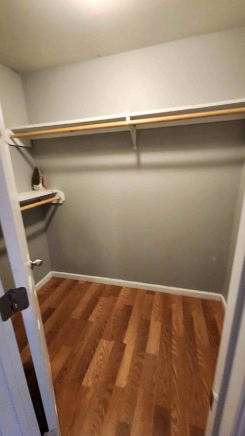 A small closet with a white door and wood flooring.