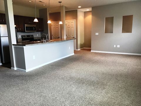 an empty living room with a kitchen and a carpeted floor