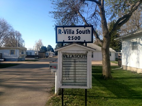 A sign for R-Villa South 2500 stands in front of a tree.