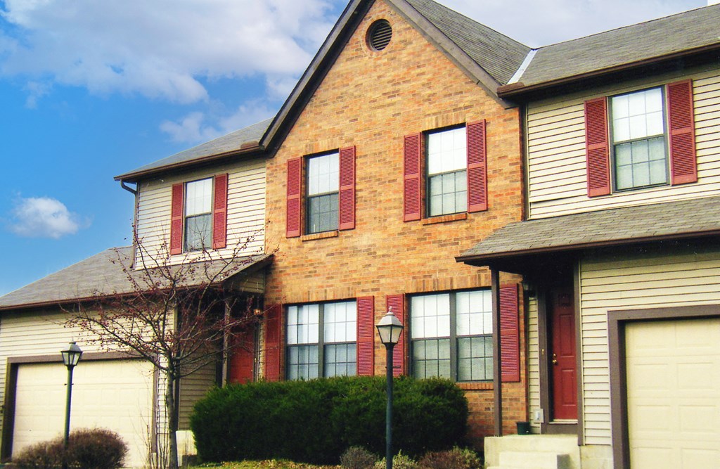 a yellow brick house with red shutters and a blue sky