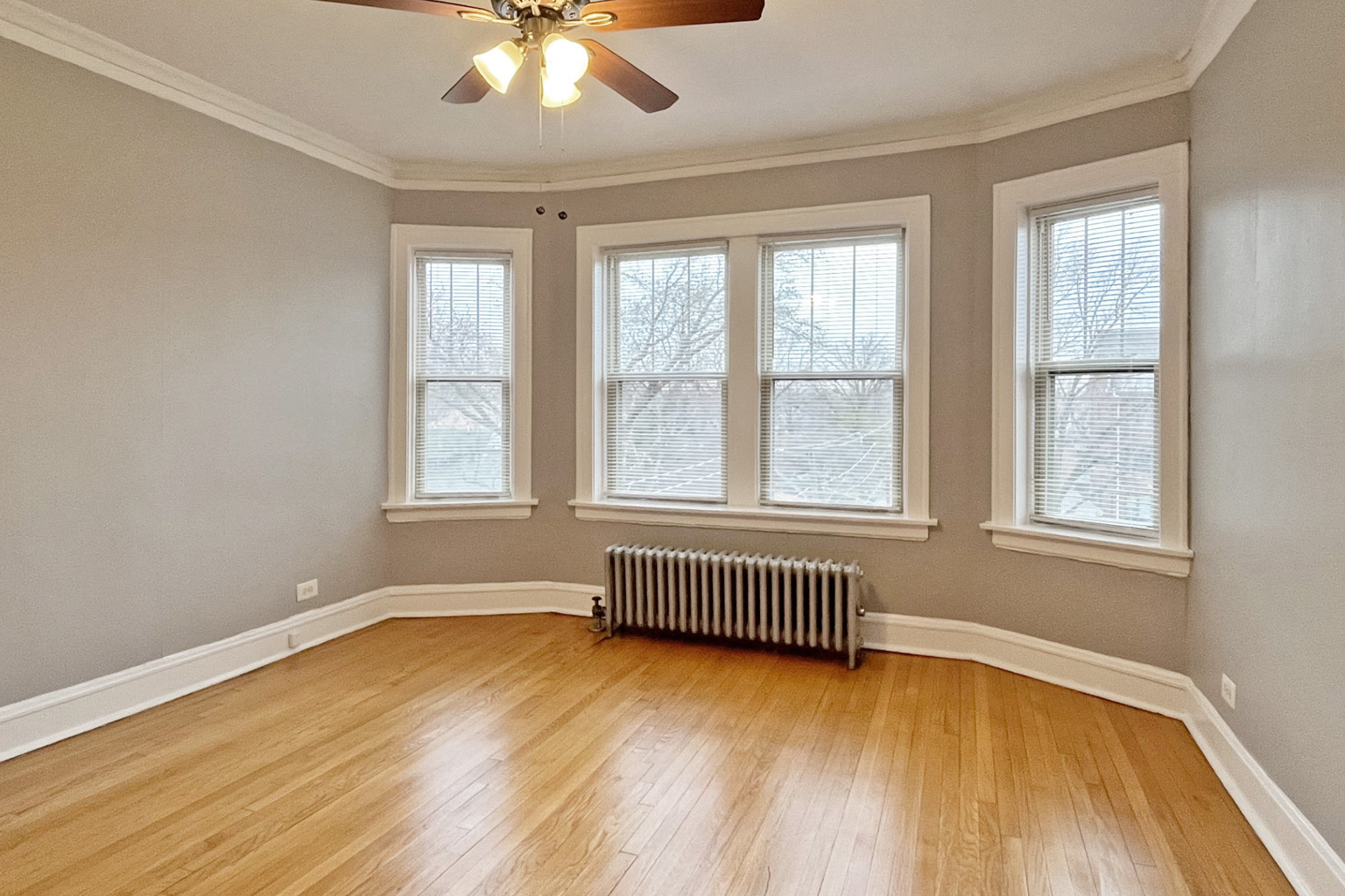 A room with a ceiling fan and three windows.