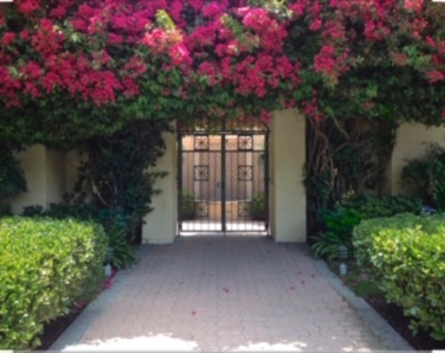 A pathway leads to a gate surrounded by greenery and pink flowers.