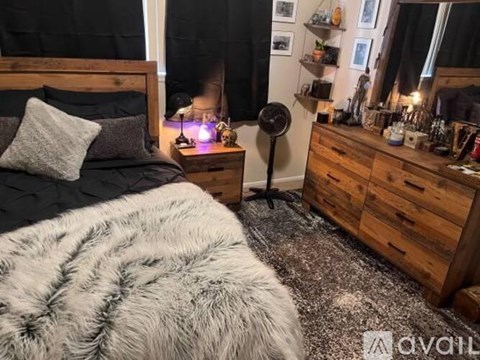 A bedroom with a black bedspread and a grey furry blanket.