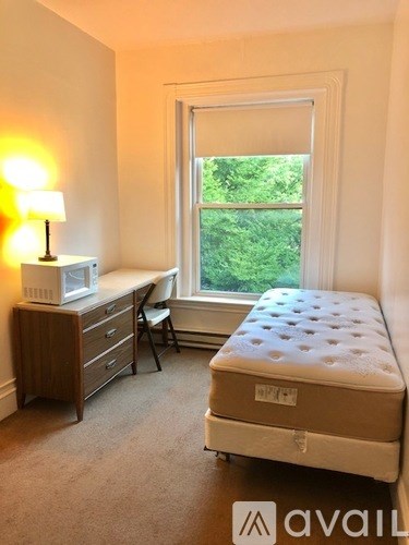 A bedroom with a bed, desk, chair, and window.
