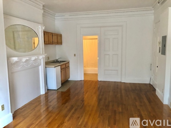 A room with wooden floors and white walls, with a large white cabinet and a round mirror on the wall.