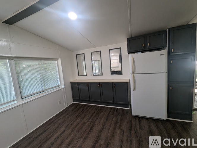 A kitchen area with a white fridge, black cupboards, and a window with blinds.