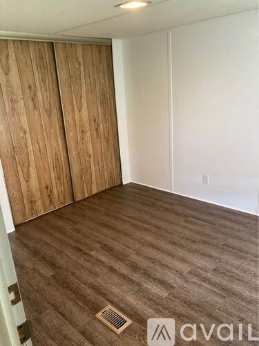 A room with wooden flooring and a white wall with a door.