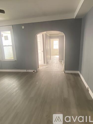 A room with grey walls and wooden flooring with a window on the left side.