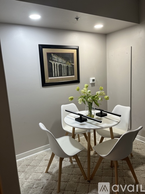 A white dining table with four chairs and a vase of flowers on top.