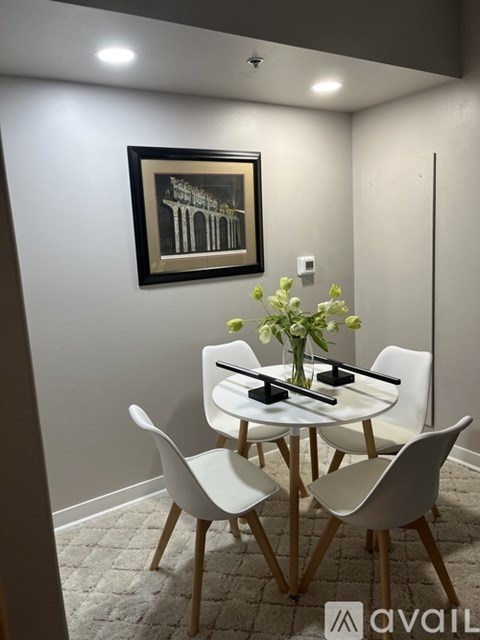 A white dining table with four chairs and a vase of flowers on top.