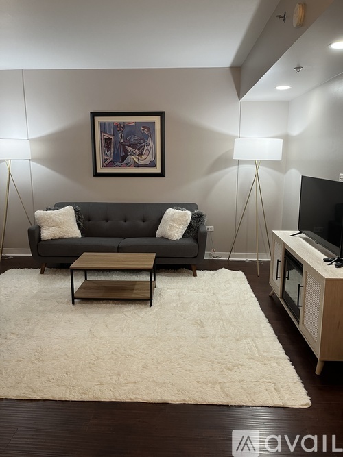 A living room with a grey couch, a white rug, and a painting on the wall.