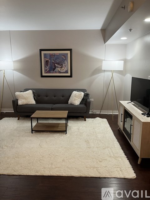 A living room with a grey couch, a white rug, and a painting on the wall.