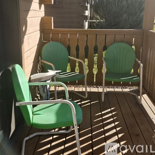 Two green chairs and a table are on a wooden deck.