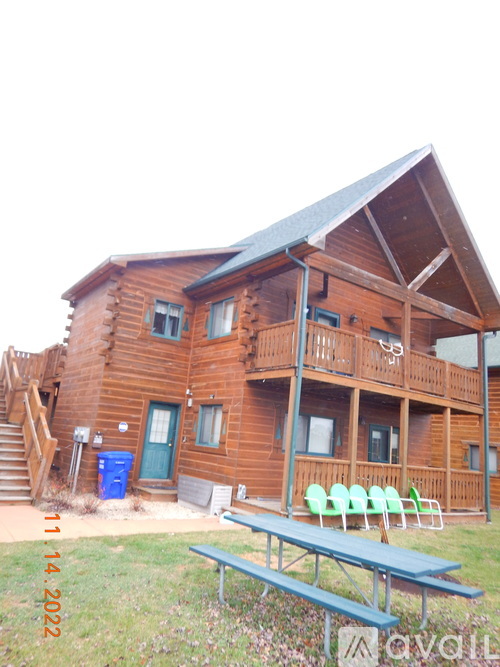 A wooden cabin with a blue trash can and green chairs in front.