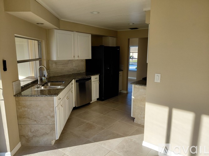 A kitchen with a black refrigerator and white cabinets.