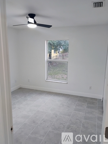 A room with a ceiling fan and a window showing a view of a street.