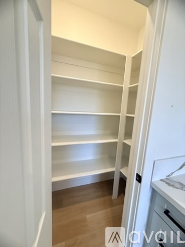 A white pantry with shelves and a wooden floor.