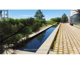A long rectangular pool surrounded by a brick walkway and trees.