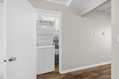 A white door opens to a kitchen with a white oven and a white fridge.