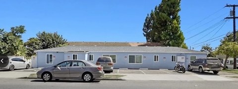 A silver car is parked in front of a grey building.