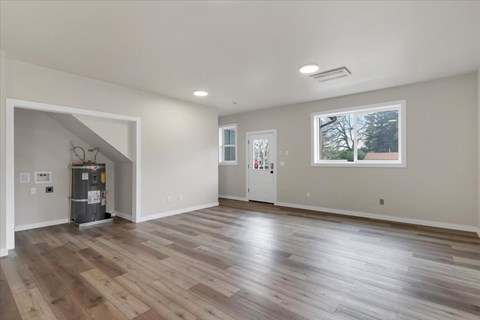 A spacious room with wooden flooring and a window overlooking a tree-lined street.