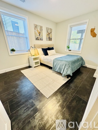 A bedroom with a bed, nightstand, and two windows.