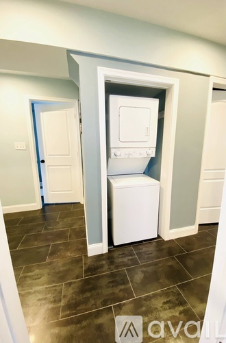 A small white refrigerator is in a narrow space between two walls.