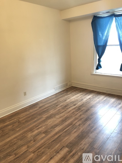 A room with wooden flooring and a window with blue curtains.