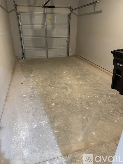 A room with a white floor and a white wall with a black trash can.
