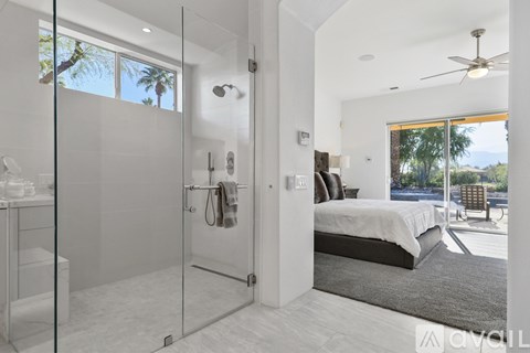 A modern bedroom with a glass shower door and a bed with a white bedspread.