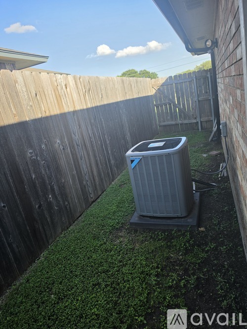 A large air conditioner unit sits on a grassy area between two wooden fences.