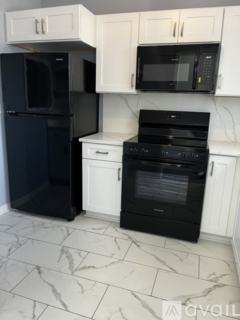 A black refrigerator and oven in a kitchen with white cabinets.
