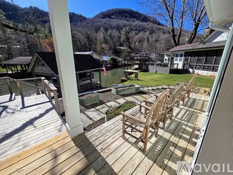 A wooden deck with chairs and a table is in the foreground with a house and trees in the background.