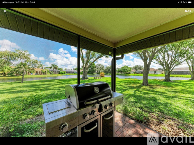 A BBQ grill is on a patio with a view of a grassy area and trees.