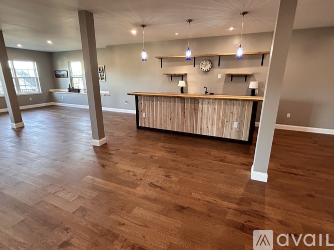 A spacious room with wooden flooring and a bar area.