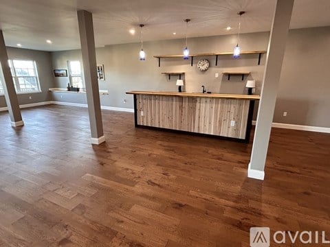A spacious room with wooden flooring and a bar area.