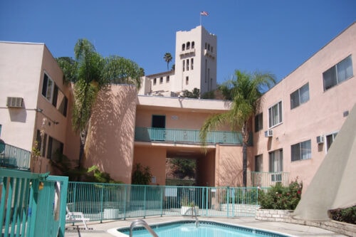 A pool in front of a pink building with a white tower.